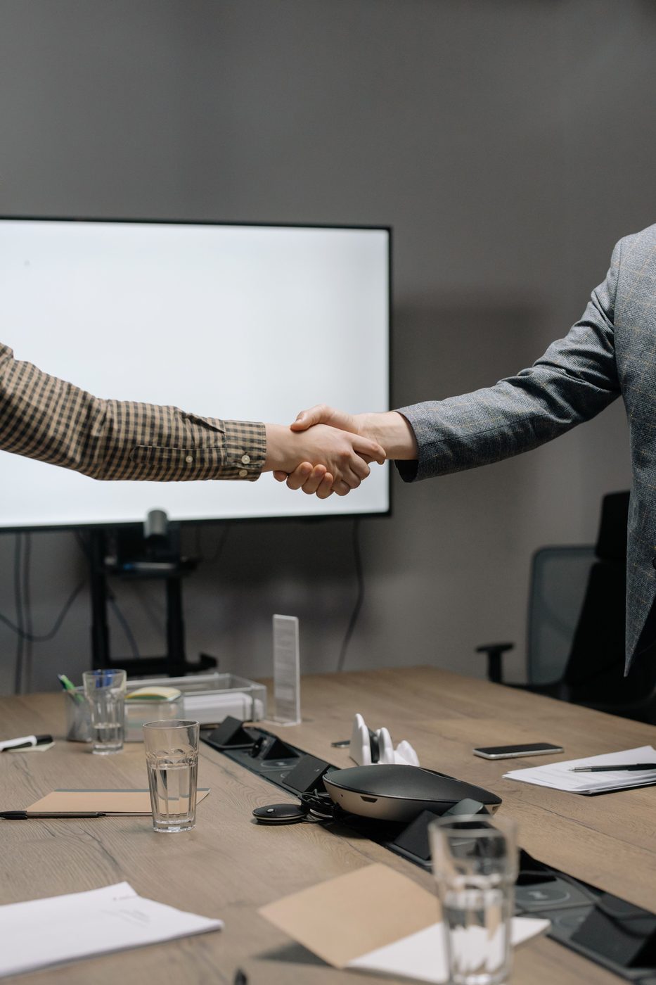 Two people shaking hands across a conference table.